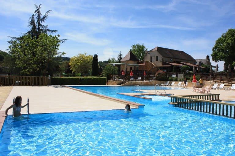 Piscine extérieure ensoleillée avec baigneurs et chaises longues.
