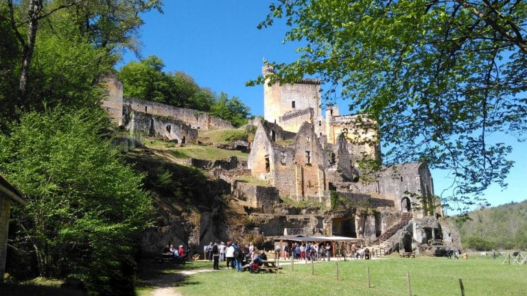 Château médiéval en ruines avec visiteurs, journée ensoleillée.