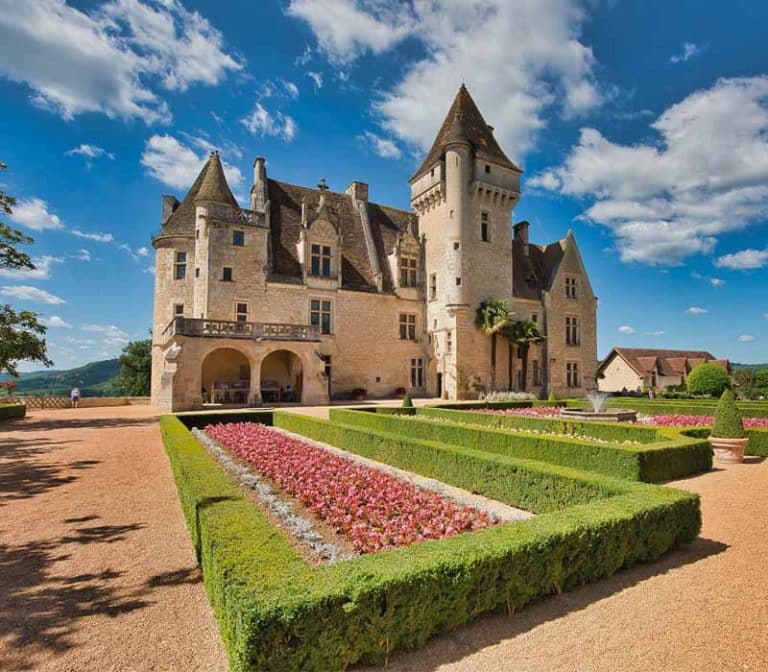 Château médiéval avec jardins fleuris, ciel bleu.