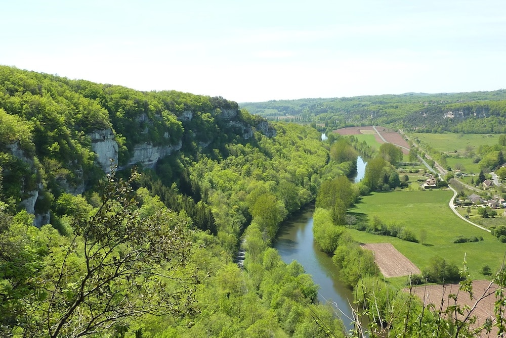 Vallée luxuriante avec rivière et falaises verdoyantes.